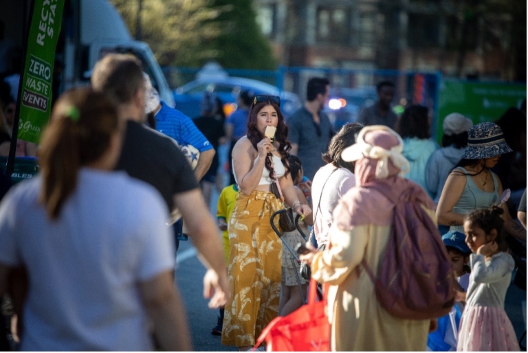 Woman eating ice cream stands alone in midst of busy crowd