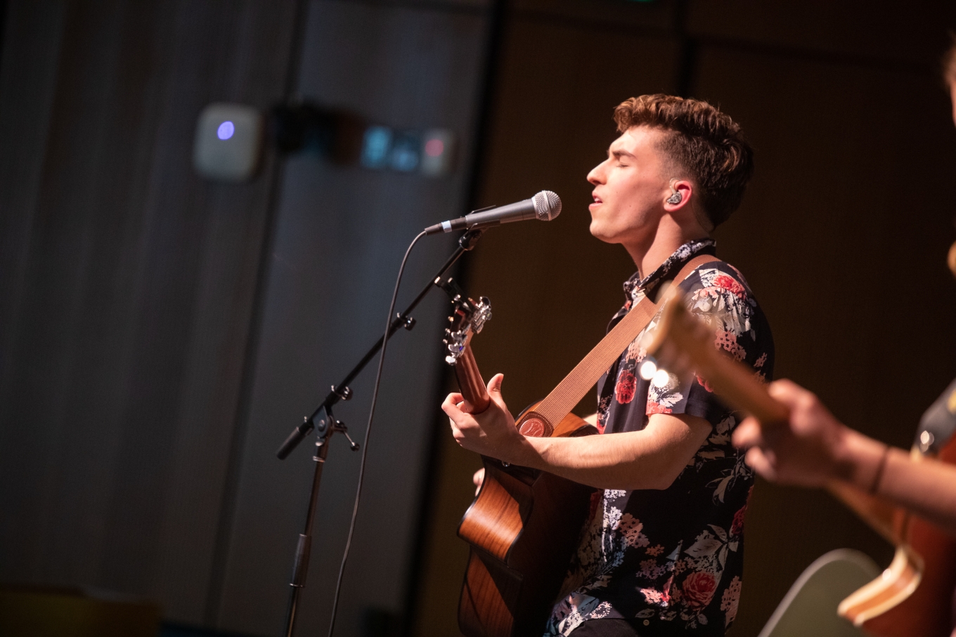 Young man performing on stage plays acoustic guitar and sings with his eyes closed 