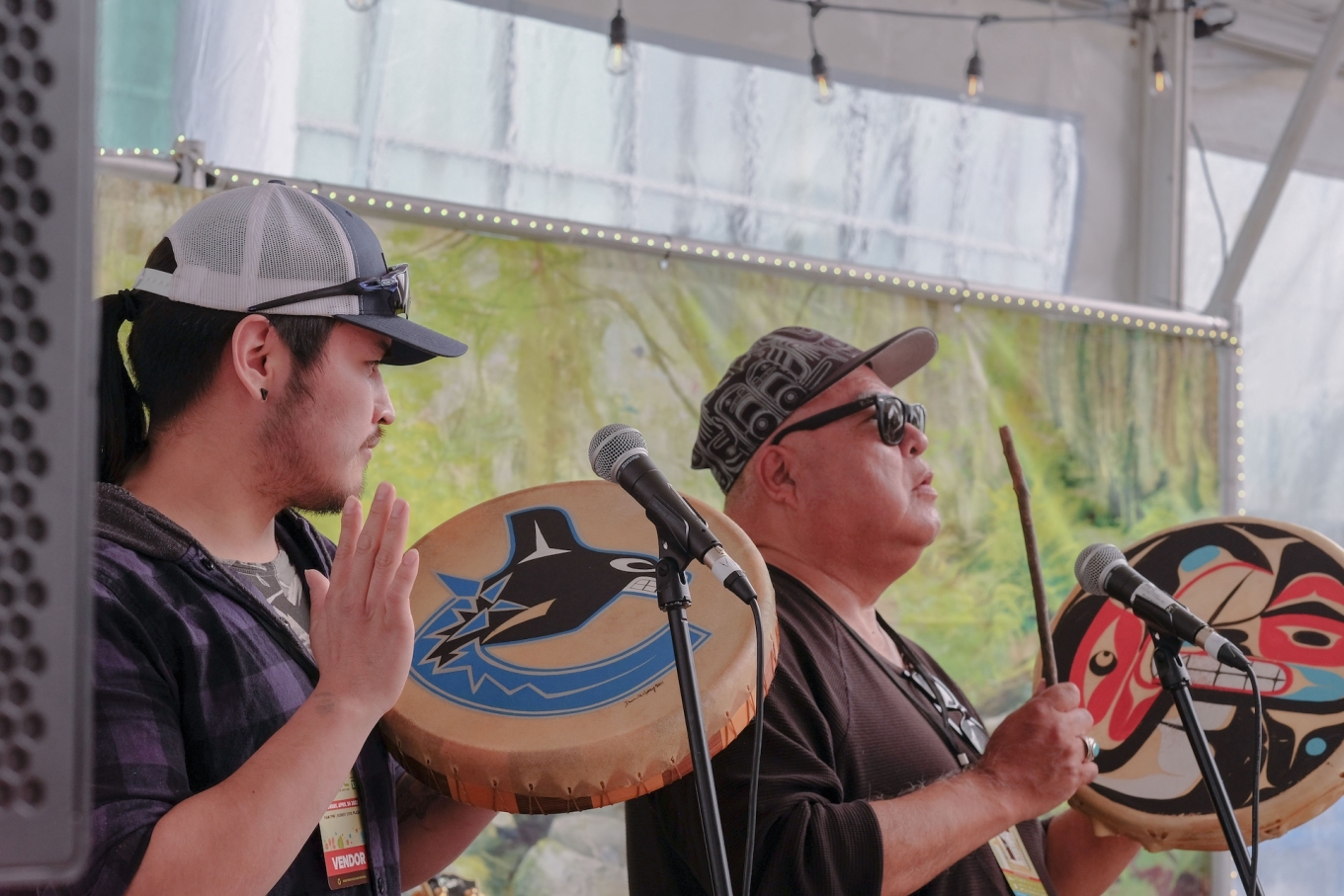 Two indigenous men singing and drumming on stage